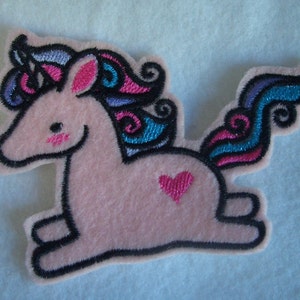 May include: Pink felt unicorn applique with a black outline, blue and pink swirls for a mane and tail, and a pink heart on its side.