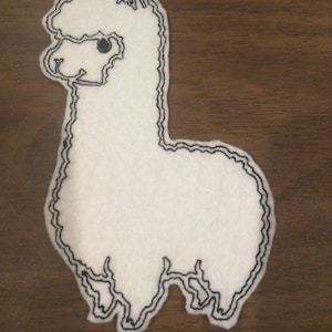 May include: White felt applique of an alpaca with black embroidered outlines. The alpaca is facing left and has a single black eye.