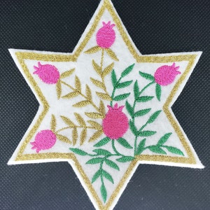 Peut inclure: Une étoile de David en feutre blanc avec un contour doré et des feuilles vertes et des grenades roses brodées.