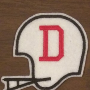 May include: White felt football helmet patch with a black outline and a red felt letter "D" in the center.