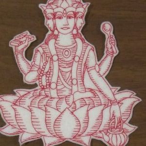 May include: Red embroidered patch of a four-armed deity with three faces sitting on a lotus flower. The deity is wearing a crown and holding a spoon, a string of beads, a book, and a teapot.