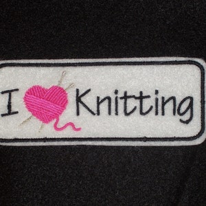 May include: White rectangular patch with black embroidered text "I love Knitting" and a pink heart with two knitting needles.