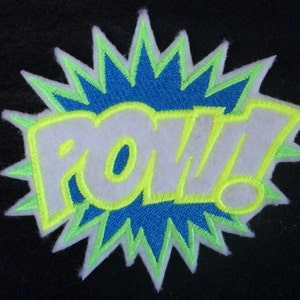 May include: A white felt patch with the word "POW!" in yellow outlined letters. The patch is surrounded by a blue and green starburst.