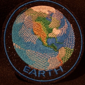 May include: Embroidered patch of a blue and green Earth with the word "EARTH" in blue lettering on a black background.