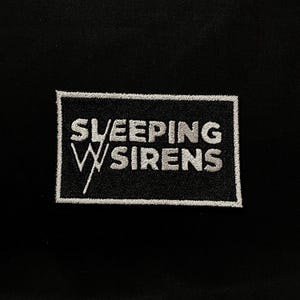 Peut inclure: Écusson brodé avec le texte "SLEEPING SIRENS" en blanc, dans un cadre rectangulaire blanc, sur fond noir. Le patch présente un "W" stylisé blanc, positionné entre les mots. Idéal pour les vêtements ou accessoires.