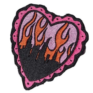 Può includere: Una toppa a forma di cuore rosa con contorno nero e un design di fiamme rosa e arancioni all'interno.
