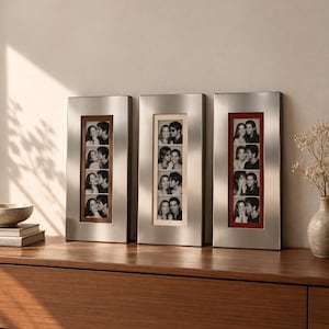 May include: Three vertical rectangular photo frames with a brushed silver metal finish. Each frame contains a strip of four black and white photographs of a couple. The frames feature inner matting in brown, cream, and red colors respectively.