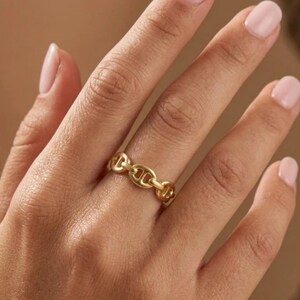 Peut inclure: Une bague dorée avec un motif de chaîne. La bague est portée au doigt, mettant en valeur ses détails et sa finition polie. Les maillons sont espacés de manière uniforme, créant un motif continu.