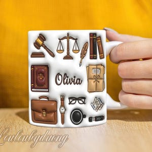 May include: White ceramic mug featuring illustrations of law-related items such as a gavel, scales, books, and a briefcase. The name "Olivia" is printed on the mug. The mug has a white handle and is held by a person.