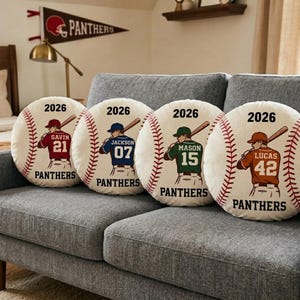 May include: Four baseball-themed throw pillows with personalized designs. Each pillow features a baseball design with a player illustration, the year "2026", and the team name "Panthers". The players' names and numbers are displayed on the jerseys.