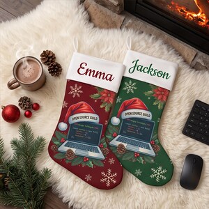 May include: Two Christmas stockings, one red and one green, featuring a white cuff with the names Emma and Jackson. Each stocking displays a laptop graphic wearing a Santa hat with the text Open Source Guild, surrounded by pine and snowflakes.