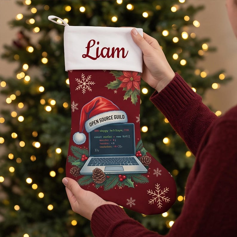 May include: A deep red Christmas stocking with a white cuff personalized with the name Liam. The stocking features a graphic of a laptop wearing a Santa hat, surrounded by pine branches, pinecones, poinsettias, and snowflakes.