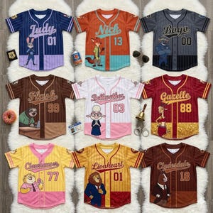 May include: Nine baseball-style jerseys in various colours, each with a character name and number. The jerseys feature illustrations of characters and unique designs. The colours include blue, orange, grey, brown, white, yellow, and maroon.