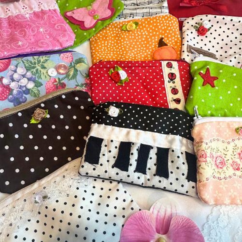 Puede incluir: Una colecci&oacute;n de bolsas de tela hechas a mano en varios colores y patrones. Los dise&ntilde;os incluyen lunares, estampados florales y detalles aplicados como mariposas, estrellas y notas musicales. Cada bolsa tiene cierre de cremallera y adornos.