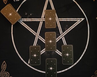 Op de afbeelding: Een zwarte tarotdoek met een wit pentagramontwerp en verschillende rechthoekige tarotkaarten. De kaarten hebben een sterontwerp. De doek is versierd met gouden Keltische knoopmotieven.