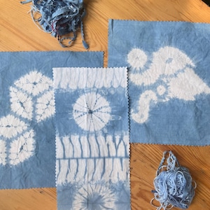 May include: Three pieces of light blue fabric with white shibori-style tie-dye patterns, including two square pieces and one rectangular strip with pinked edges, accompanied by two loose bundles of matching light blue fabric strips.