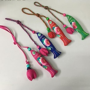 以下が含まれることがあります： カラフルな魚の形をした布製オーナメントのコレクション。各オーナメントには刺繍された花の模様があり、タッセルとビーズコードが付いています。魚はピンク、青、赤、緑など様々な色があり、タッセルも同様の色です。
