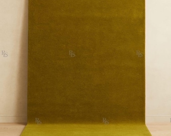 Könnte beinhalten: Ein rechteckiger, olivgrüner Teppich mit weicher, strukturierter Optik. Der Teppich ist vor einer neutralfarbenen Wand platziert und erstreckt sich auf einen hellen Holzboden. Die Farbe des Teppichs ist durchgehend, wodurch ein nahtloser Look entsteht.