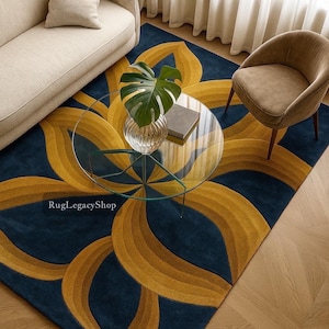 Puede incluir: Una alfombra azul marino con un gran diseño floral estilizado en tonos dorados y amarillos. Una mesa de centro de cristal transparente con marco de metal verde se encuentra sobre la alfombra, junto con un sofá beige y un sillón marrón. El diseño de la alfombra recuerda a una flor.