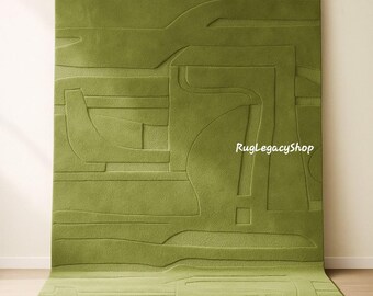 May include: A large, rectangular green rug with a raised, abstract design. The rug features a series of curved and geometric shapes in varying heights, creating a textured surface. The rug is displayed on a light-colored floor and against a neutral wall.
