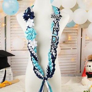 May include: A graduation lei in blue, white, and navy ribbons, adorned with fabric flowers and a "Class of 2026" charm. The lei features the letters "Y F D F" in white with a black outline. The lei is displayed on a mannequin.
