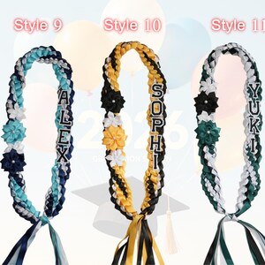 May include: Three graduation leis in the image. Each lei is braided with ribbons in various colors, including blue, white, black, yellow, and green. Each lei has a name spelled out in individual letters. Floral accents and ribbons complete the design.
