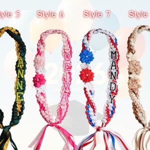May include: Four graduation leis in various styles. Each lei is braided with colorful ribbons and adorned with decorative flowers and personalized name tags. Styles include green, pink, red, and brown.