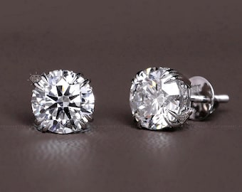 May include: A pair of sparkling diamond stud earrings. Each earring features a round-cut diamond set in a silver or white gold setting. The earrings are displayed on a brown background, showcasing their brilliance.