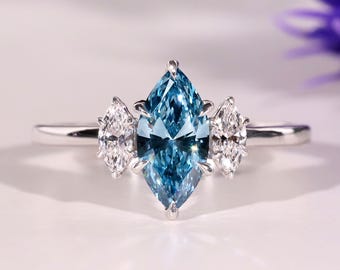 May include: A marquise-cut, light blue gemstone ring with two smaller white gemstones on either side. The ring is set in a silver band. The ring is displayed on a white surface.