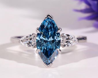 May include: A marquise-cut, light blue gemstone ring with two pear-shaped white gemstones on either side. The ring is set in a silver band. The ring is displayed on a white surface.