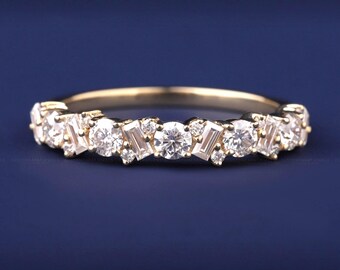 May include: A gold band ring with a series of round and baguette-cut diamonds. The diamonds are set in a cluster pattern, creating a sparkling effect. The ring is set against a dark blue background.