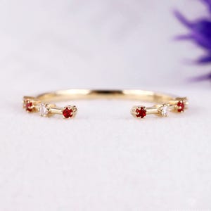 May include: A fine gold ring adorned with alternating red and clear gemstones. The ring has a slim band and is set with small, round gemstones. The gemstones are evenly spaced around the ring, creating a simple and elegant design.