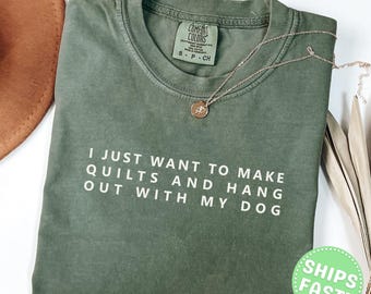 Może przedstawiać: Mchowo-zielony t-shirt z krótkim rękawem, okrągłym dekoltem i białym nadrukiem I JUST WANT TO MAKE QUILTS AND HANG OUT WITH MY DOG. Koszulka posiada metkę marki Comfort Colors przy wewnętrznym kołnierzyku oraz cienki złoty naszyjnik.