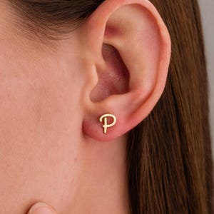 May include: A gold initial letter 'P' earring. The earring is worn in the left earlobe.