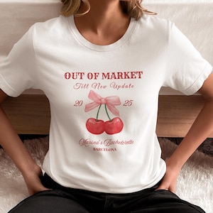 Puede incluir: Camiseta blanca con un gráfico rojo de dos cerezas con un lazo rosa y el texto "Out of Market Till New Update 20 25 Marina's Bachelorette Barcelona".