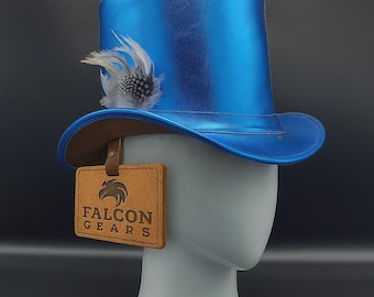 May include: A vibrant blue top hat with a brown brim and a decorative feather. A leather tag with the words "FALCON GEARS" hangs from the hat. The hat is displayed on a mannequin head.