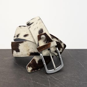 May include: A white ceramic mug with a black handle and the text "But First, Coffee" in a bold, black font. The mug is set against a blurred background, highlighting its clean design.