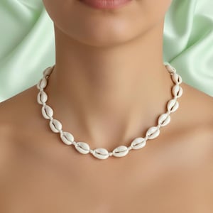 May include: A necklace made of white cowrie shells. The shells are strung together with a white cord, creating a delicate and natural look. The necklace is a simple yet elegant piece of jewellery.