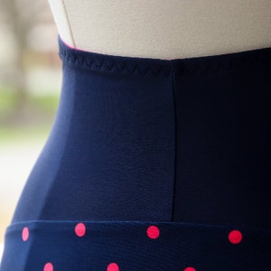 Puede incluir: Primer plano de la cintura de una falda azul marino con estampado de lunares rosas. La cintura es de color azul marino s&oacute;lido con una costura rosa.