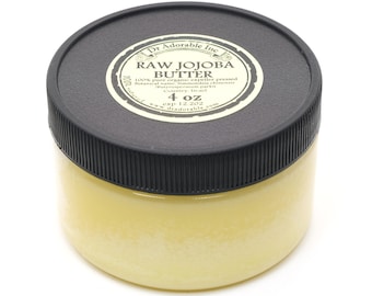 May include: A black jar with a white label that reads "Dr. Adorable Inc. Raw Jojoba Butter 100% pure organic expeller pressed Botanical name: Simmondsia chinensis Butyrospermum parki Country: Israel 4 oz exp 12.202 www.dradorable.com". The jar is filled with a yellow substance.