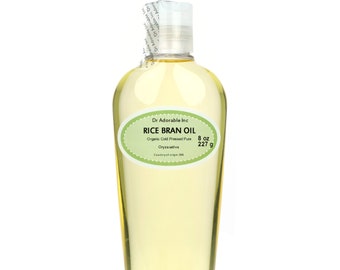 May include: A clear plastic bottle filled with yellow rice bran oil. The label reads "Dr Adorable Inc RICE BRAN OIL Organic Cold Pressed Pure 8 oz 227 g". The bottle has a white cap and a tamper-evident seal.