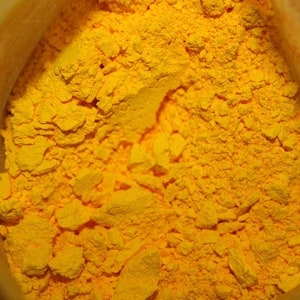 May include: A close-up view of a bag of bright yellow powder. The powder is finely ground and has a slightly grainy texture.