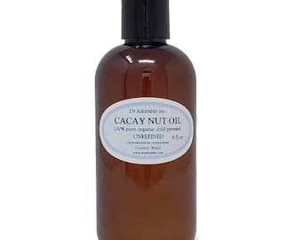 Puede incluir: Una botella de vidrio marrón con una tapa negra que contiene 237 ml de aceite de nuez de cacay. La etiqueta es blanca con texto azul y dice "Dr. Adorable inc Cacay Nut Oil 100% pure organic cold pressed Unrefined Caryodendron orinocense Country Brazil www.dradorable.com 8 floz".