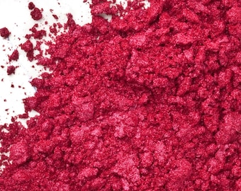 May include: Close-up of a pile of loose, red glitter. The glitter is a deep, rich red color and has a slight shimmer.