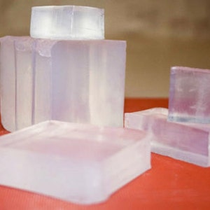 May include: Four clear, rectangular bars of soap. The bars are stacked on top of each other, with the largest bar on the bottom and the smallest bar on top. The bars are all made of the same type of soap, and they are all translucent.