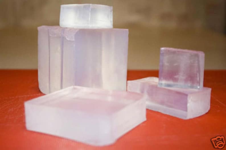 May include: Four clear, rectangular bars of soap. The bars are stacked on top of each other, with the largest bar on the bottom and the smallest bar on top. The bars are all made of the same type of soap, and they are all translucent.