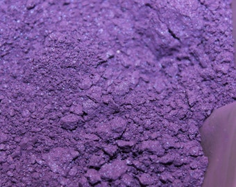 May include: A close-up of a purple powder with a slight shimmer. The powder is in a container, but the container is not visible in the image.