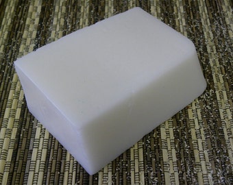 May include: A white rectangular bar of soap on a brown and white woven mat.