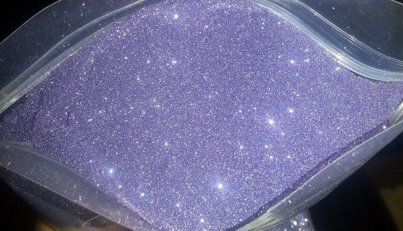 May include: A close-up view of a bag of purple glitter. The glitter is fine and sparkly, and it is perfect for crafting or decorating.