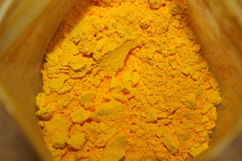 May include: A close-up view of a bag of bright yellow powder. The powder is finely ground and has a slightly grainy texture.